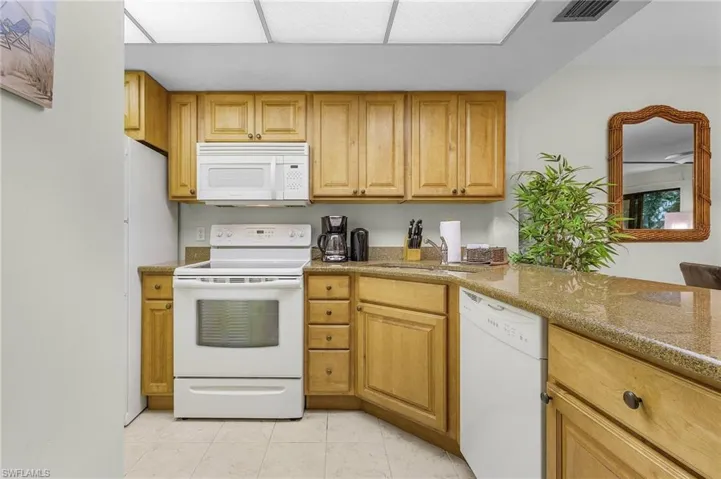 Kitchen with light stone counters, white appliances, and sink