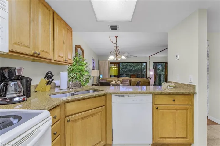 Kitchen featuring kitchen peninsula, ceiling fan with notable chandelier, white appliances, sink, and light brown cabinets