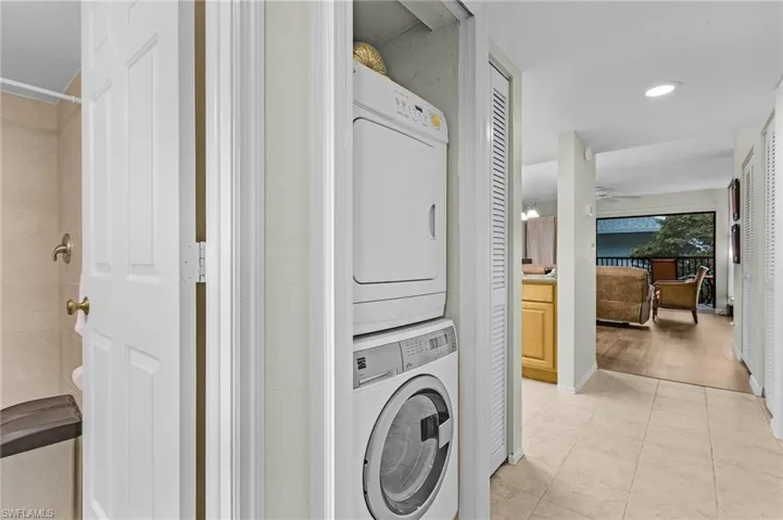 Clothes washing area featuring light tile patterned floors, stacked washing maching and dryer, and ceiling fan
