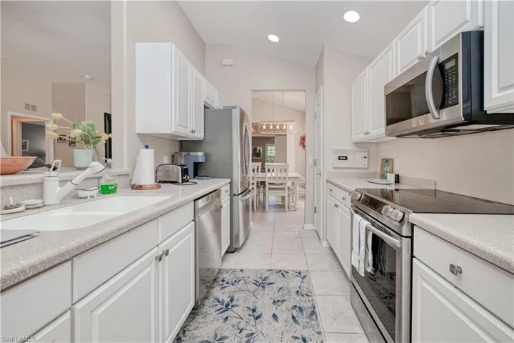 Kitchen featuring vaulted ceiling, light tile flooring, white cabinetry, appliances with stainless steel finishes, and sink