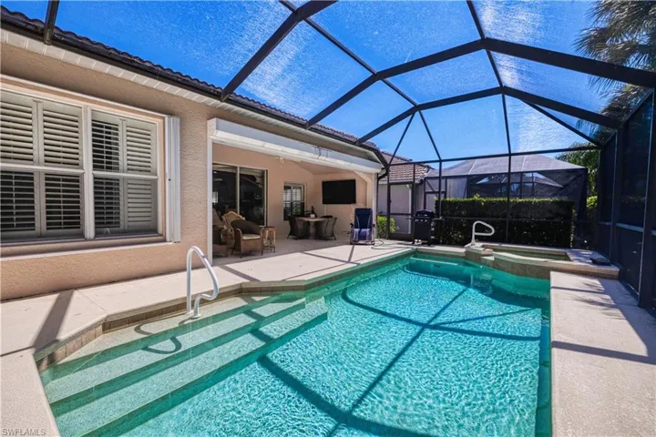 View of pool featuring a patio area, glass enclosure, and an in ground hot tub