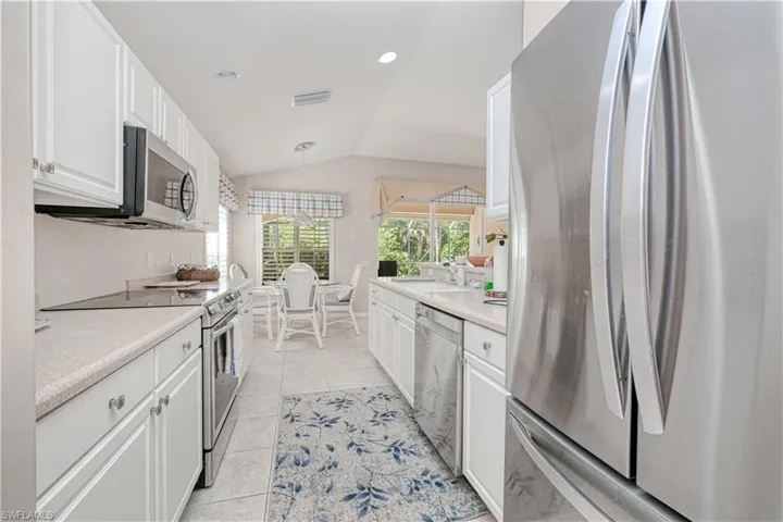 Kitchen with hanging light fixtures, appliances with stainless steel finishes, white cabinets, light tile flooring, and vaulted ceiling