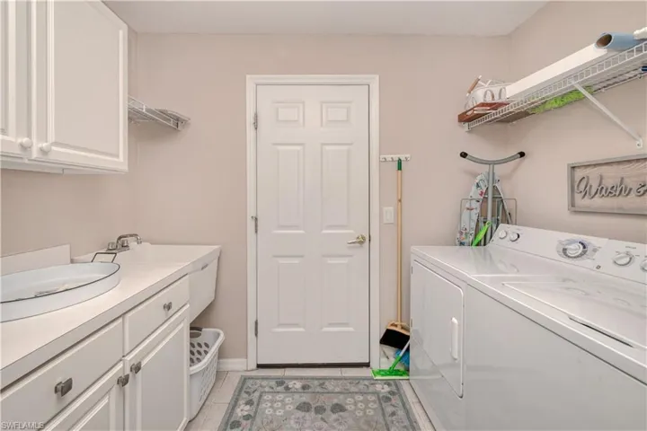 Laundry room featuring cabinets, sink, light tile floors, and washing machine and clothes dryer