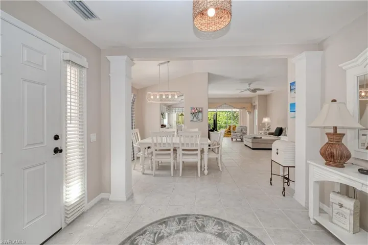 Tiled foyer entrance with ornate columns and ceiling fan with notable chandelier