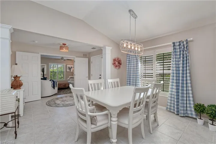 Tiled dining room featuring ornate columns, vaulted ceiling, and ceiling fan with notable chandelier