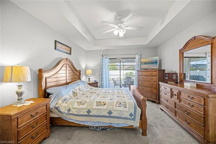 Bedroom featuring access to exterior, a tray ceiling, light colored carpet, and a ceiling fan