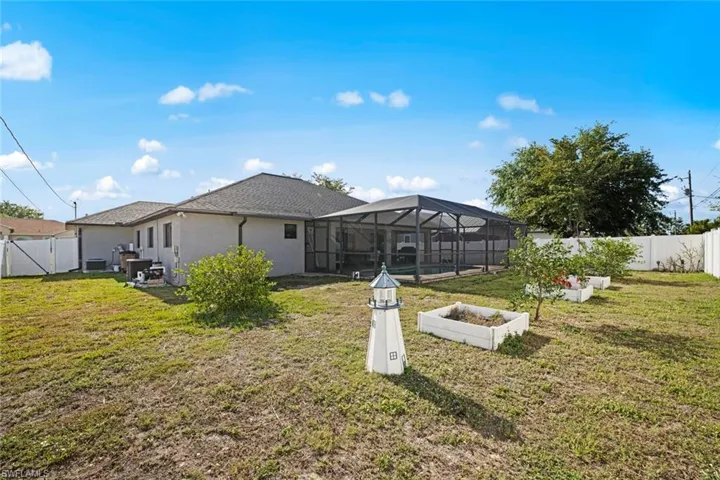 Rear view of property with a vegetable garden, a lawn, a fenced backyard, stucco siding, and a lanai