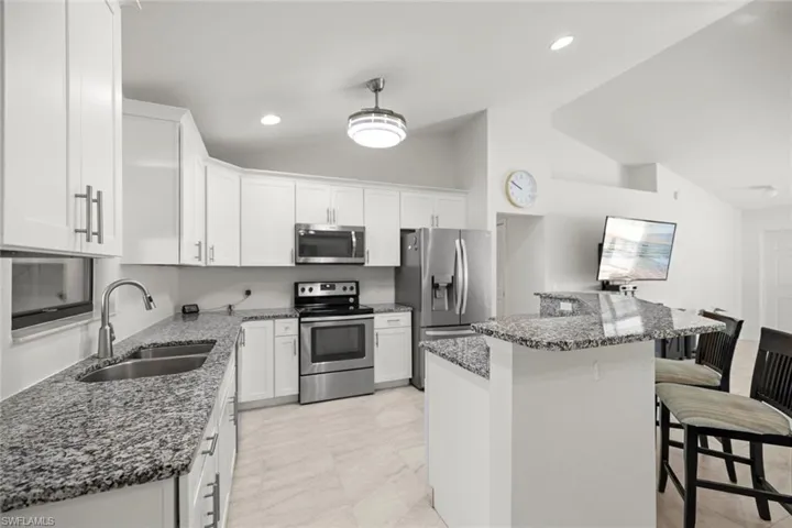 Kitchen with dark stone countertops, white cabinets, a sink, a kitchen breakfast bar, and stainless steel appliances
