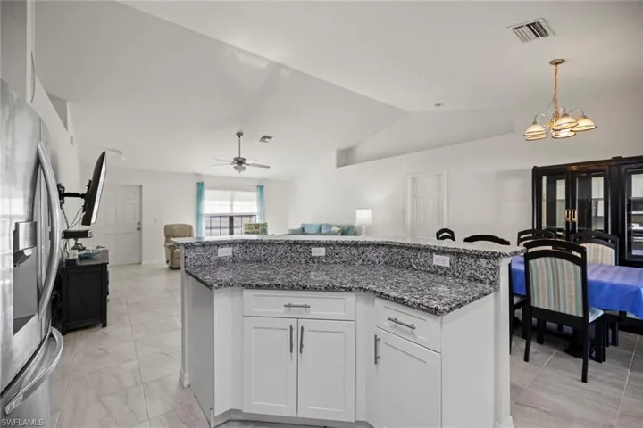 Kitchen with stainless steel fridge with ice dispenser, visible vents, open floor plan, and dark stone counters