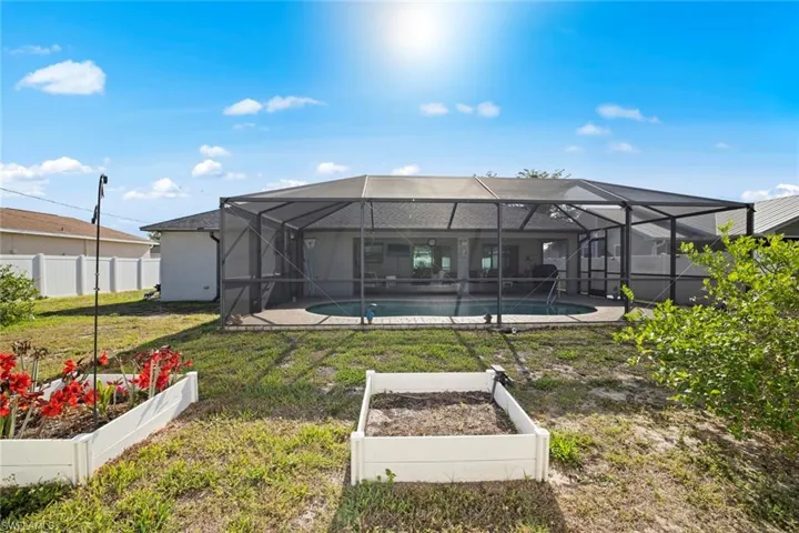 Rear view of house featuring a yard, a fenced in pool, fence, and a vegetable garden