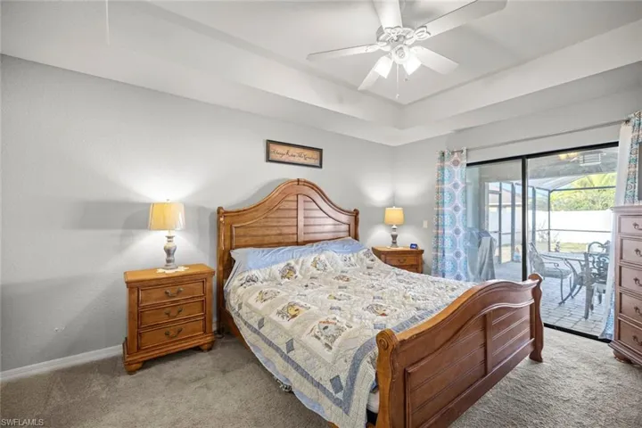 Bedroom with baseboards, a raised ceiling, access to exterior, ceiling fan, and carpet