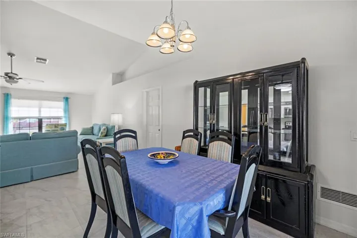 Dining space featuring ceiling fan with notable chandelier, baseboards, lofted ceiling, and visible vents