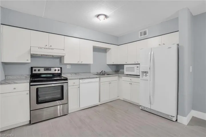 Kitchen featuring white cabinets, sink, white appliances, and light stone countertops