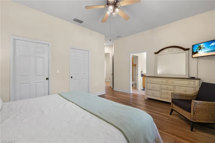 Primary Bedroom with wood-style flooring, ensuite bathroom, ceiling fan and two walk in closets.