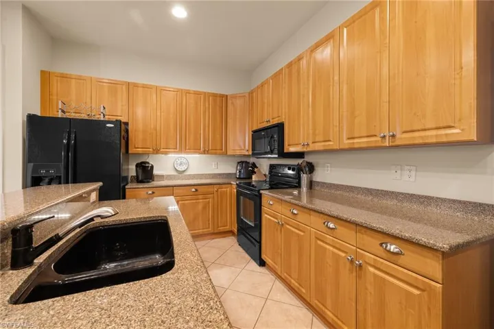 Kitchen with light granite counters, sink, light tile patterned floors, and black appliances. Plenty of counterspace for family dining and entertaining.