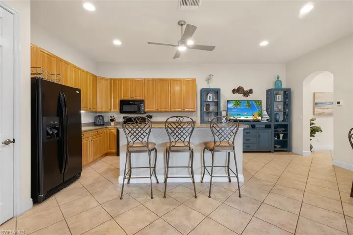 Kitchen featuring light tile patterned flooring, a kitchen breakfast bar island with sink, ceiling fan, and black appliances