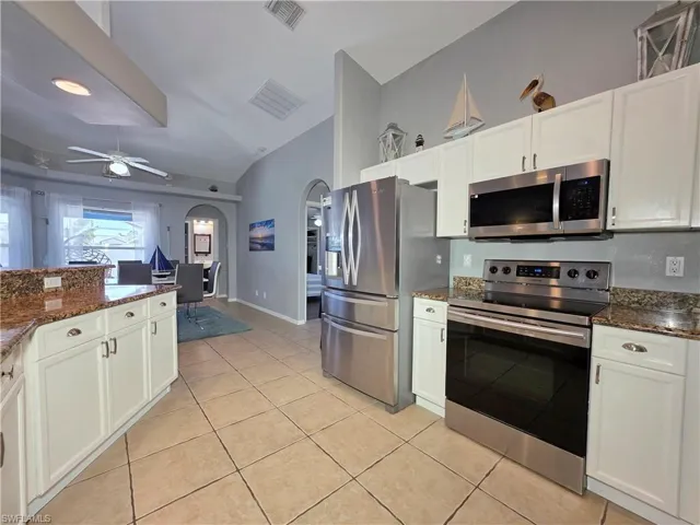 Kitchen with arched walkways, stainless steel appliances, dark stone countertops, ceiling fan, and lofted ceiling