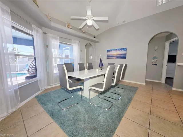 Dining room featuring light tile patterned floors, arched walkways, ceiling fan, and vaulted ceiling