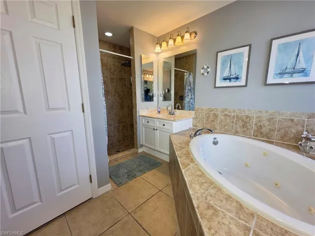 Bathroom with a whirlpool tub, vanity, light tile patterned floors, and a shower stall