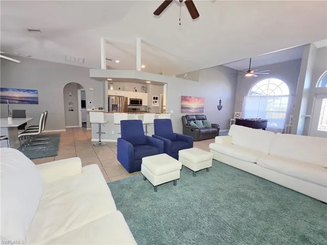 Living area with a ceiling fan, arched walkways, light tile patterned flooring, and lofted ceiling