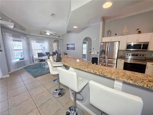 Kitchen featuring stainless steel appliances, light stone countertops, arched walkways, a breakfast bar area, and open floor plan