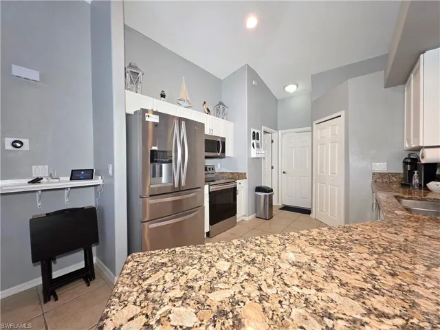Kitchen with light tile patterned floors, stainless steel appliances, white cabinetry, and light stone countertops