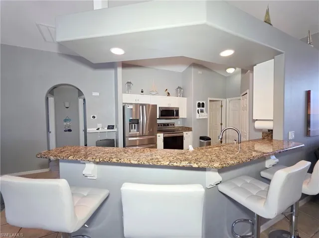 Kitchen featuring a breakfast bar area, stainless steel appliances, light stone counters, arched walkways, and vaulted ceiling