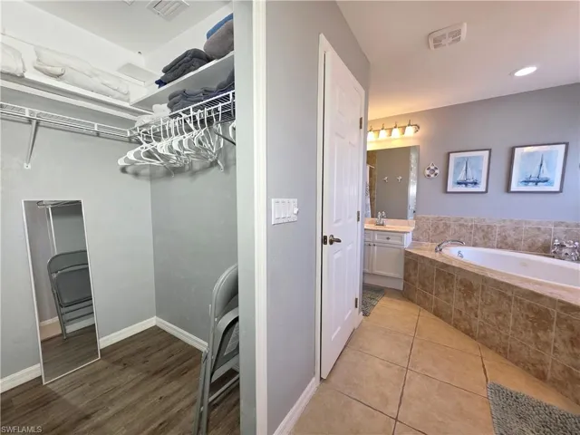 Bathroom with a spacious closet, vanity, light tile patterned flooring, and a bath