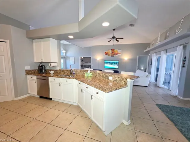 Kitchen featuring white cabinets, a peninsula, open floor plan, dark stone counters, and stainless steel dishwasher