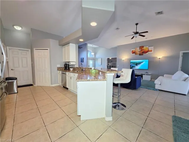 Kitchen featuring white cabinetry, a peninsula, a kitchen breakfast bar, open floor plan, and light stone countertops