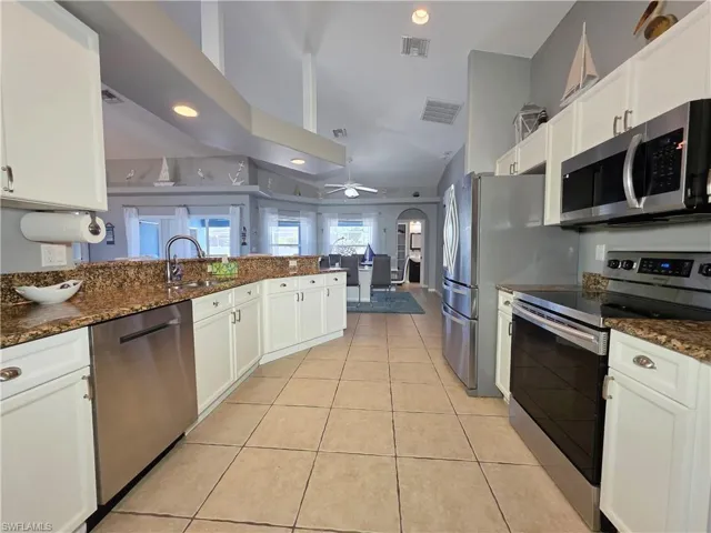 Kitchen featuring stainless steel appliances, arched walkways, dark stone counters, white cabinets, and recessed lighting