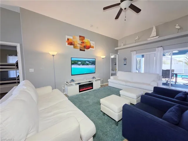 Carpeted living room with lofted ceiling, ceiling fan, and a glass covered fireplace