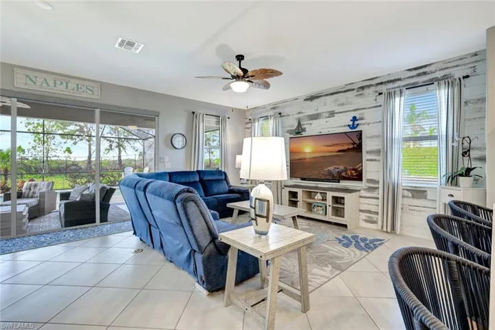 Living room featuring an accent wall, ceiling fan, visible vents, and light tile patterned floors