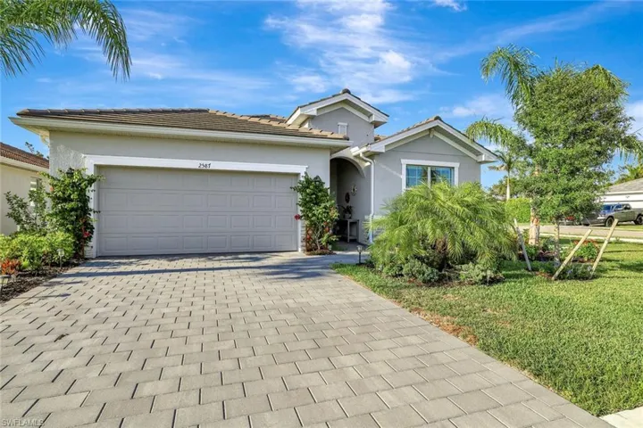 Ranch-style home featuring a garage, a tile roof, stucco siding, a front lawn, and decorative driveway