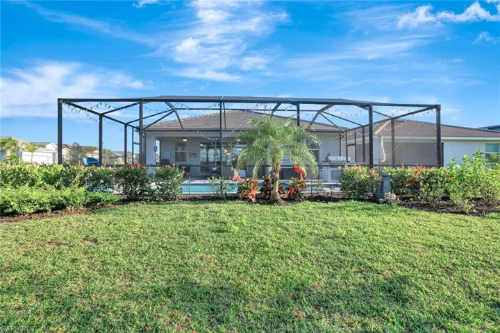 Rear view of house with an outdoor pool, stucco siding, a lanai, and a lawn