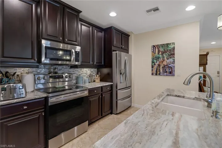 Kitchen with backsplash, a sink, light stone countertops, stainless steel appliances, and visible vents