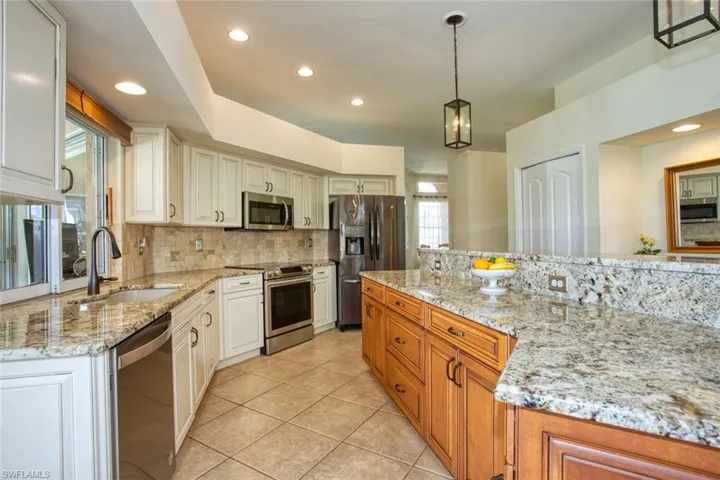 Kitchen with decorative light fixtures, white cabinets, stainless steel appliances, and sink