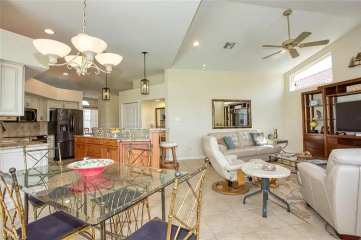 Tiled kitchen dining space with a wealth of natural light, lofted ceiling, and ceiling fan with notable chandelier
