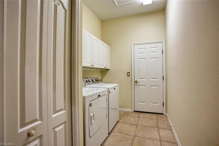 Laundry area with cabinets, washing machine and clothes dryer, and light tile patterned floors