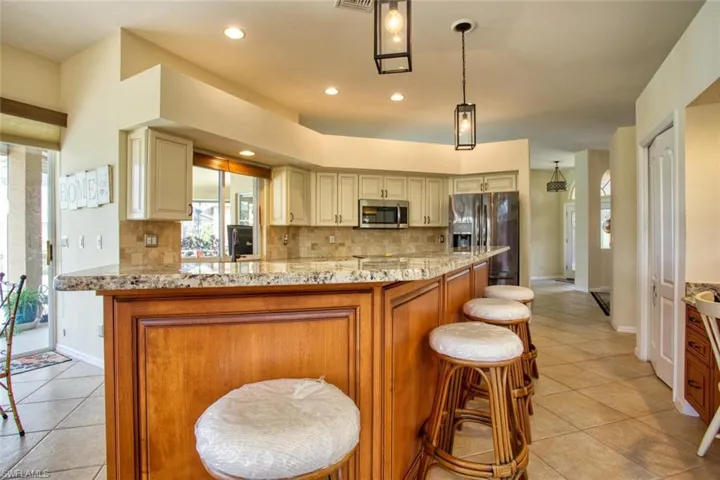 Kitchen with pendant lighting, light stone countertops, stainless steel appliances, and cream cabinets