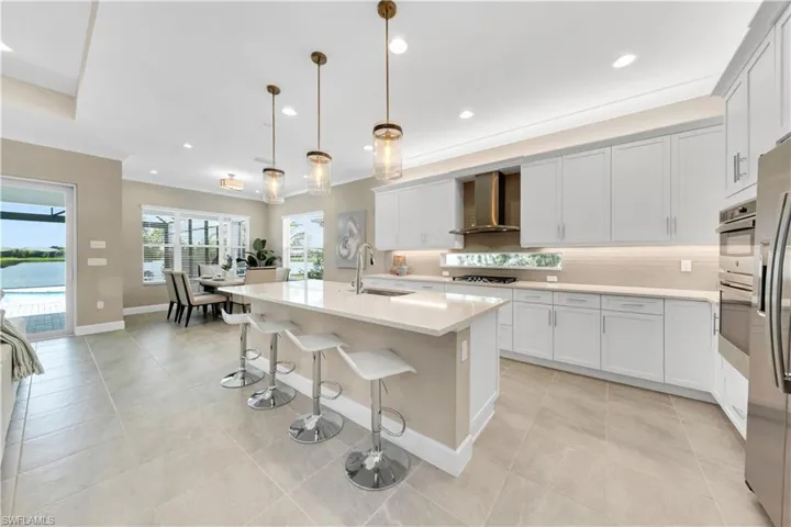 Kitchen with decorative backsplash, wall chimney exhaust hood, light tile patterned flooring, and a center island with sink