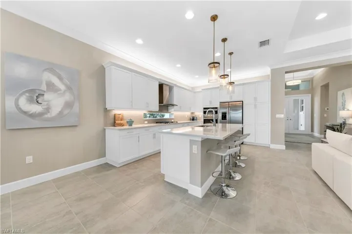 Kitchen featuring appliances with stainless steel finishes, white cabinets, an island with sink, a breakfast bar, and wall chimney exhaust hood