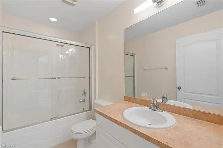 Bathroom with toilet, shower / bath combination with glass door, and vanity