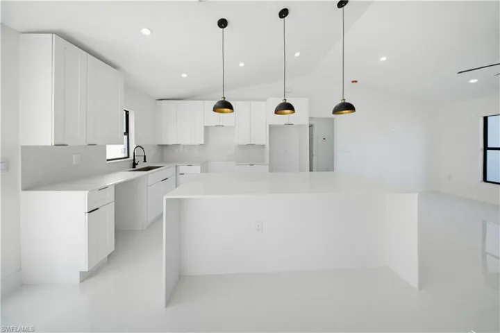 Kitchen with white cabinets, a center island, pendant lighting, light stone countertops, and recessed lighting