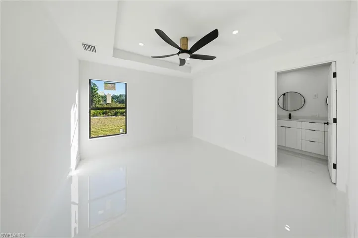 Unfurnished bedroom with a tray ceiling, a ceiling fan, recessed lighting, and ensuite bath