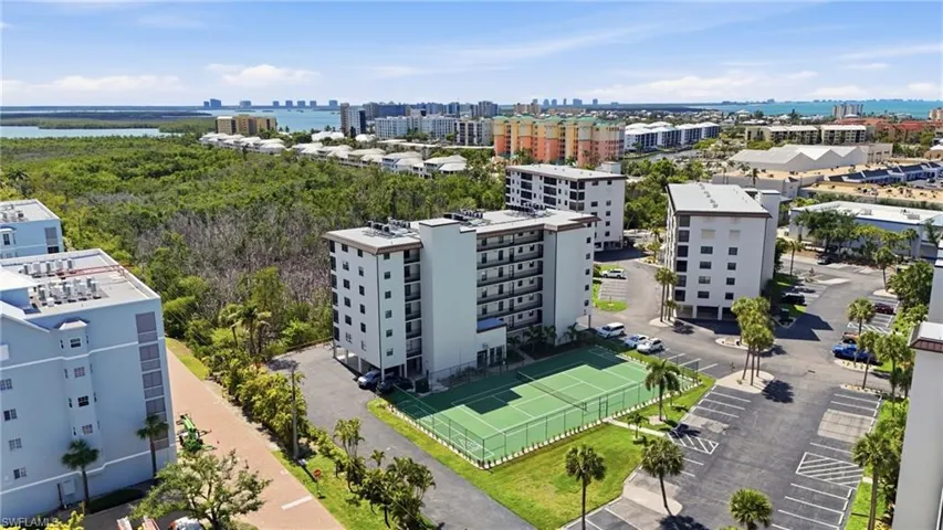 Community featuring multiple mid-rise residential buildings, a tennis court, and ample surface parking - Virtually Edited Image