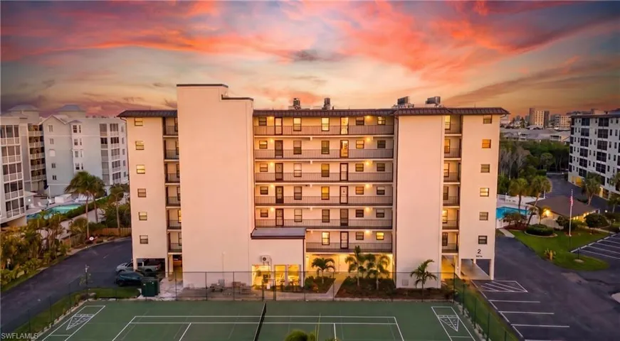 Multi-story condominium building featuring private balconies, a tennis court, and on-site parking - Virtually Edited Image
