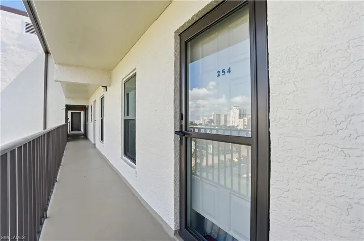 Exterior corridor with textured white stucco walls and a gray protective railing - Virtually Edited Image