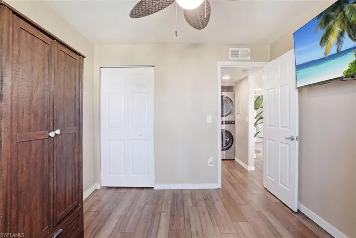 Room featuring wood-finish flooring, a ceiling fan, and a built-in wood-paneled wardrobe - Virtually Edited Image