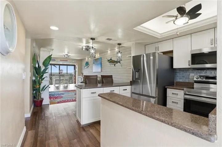 Kitchen featuring white cabinetry, stainless steel appliances, a blue subway tile backsplash, and a breakfast bar with a stone-finish countertop - Virtually Edited Image